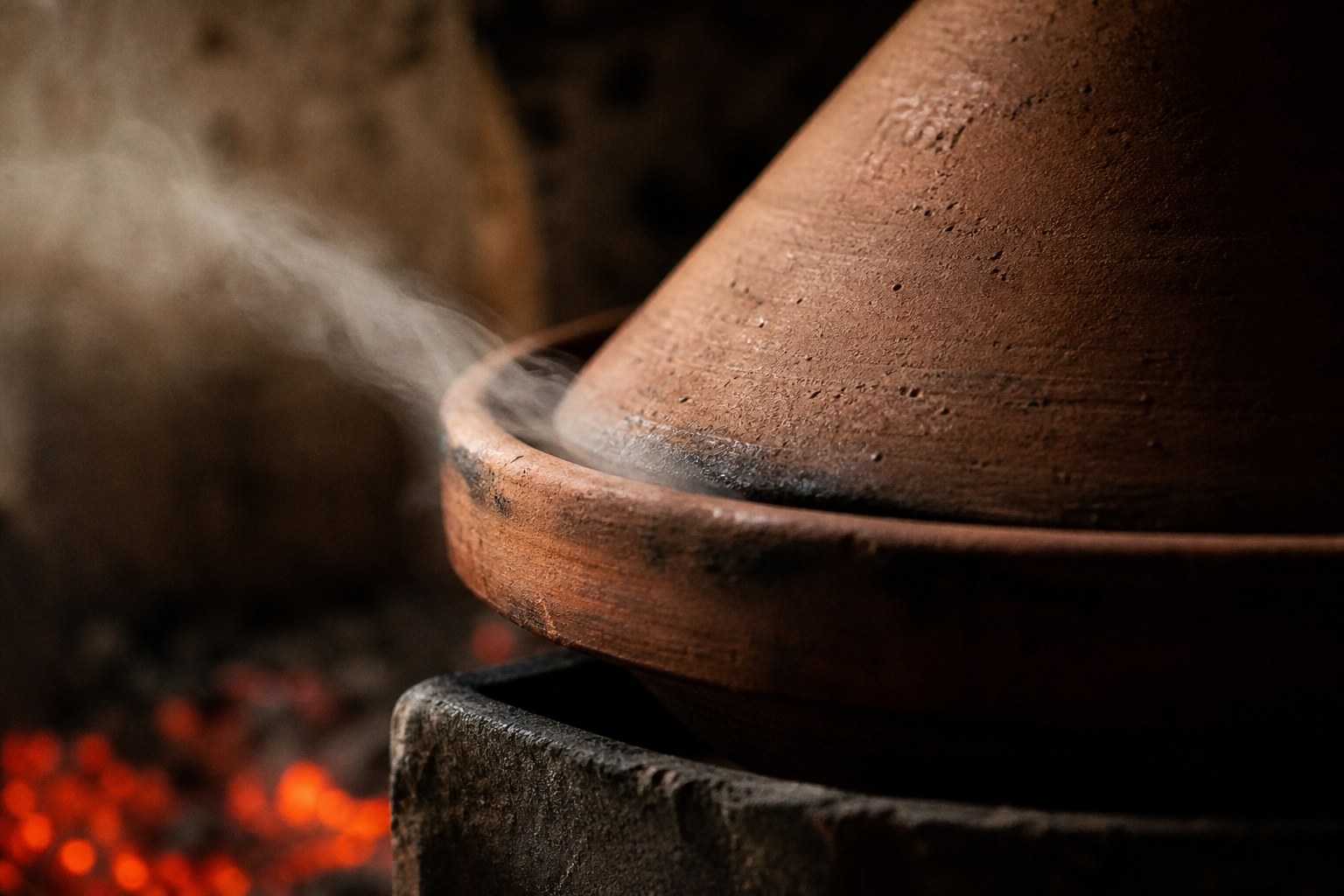 A tagine on a clay brazier, steam threading from the seam of the lid.
